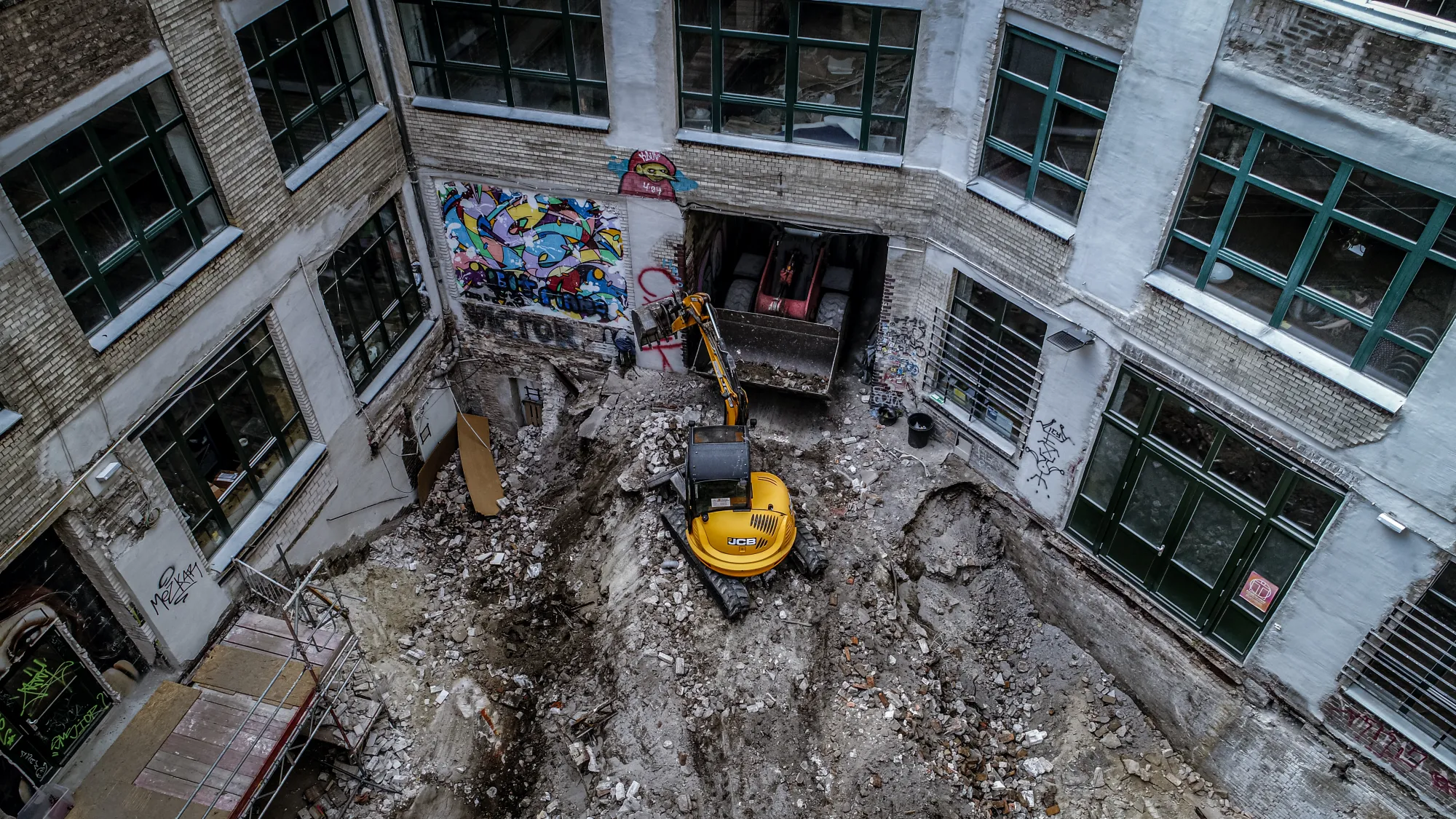 Hinterhof-Rückbau mit gelbem Minibagger in einem Berliner Innenhof, Luftaufnahme