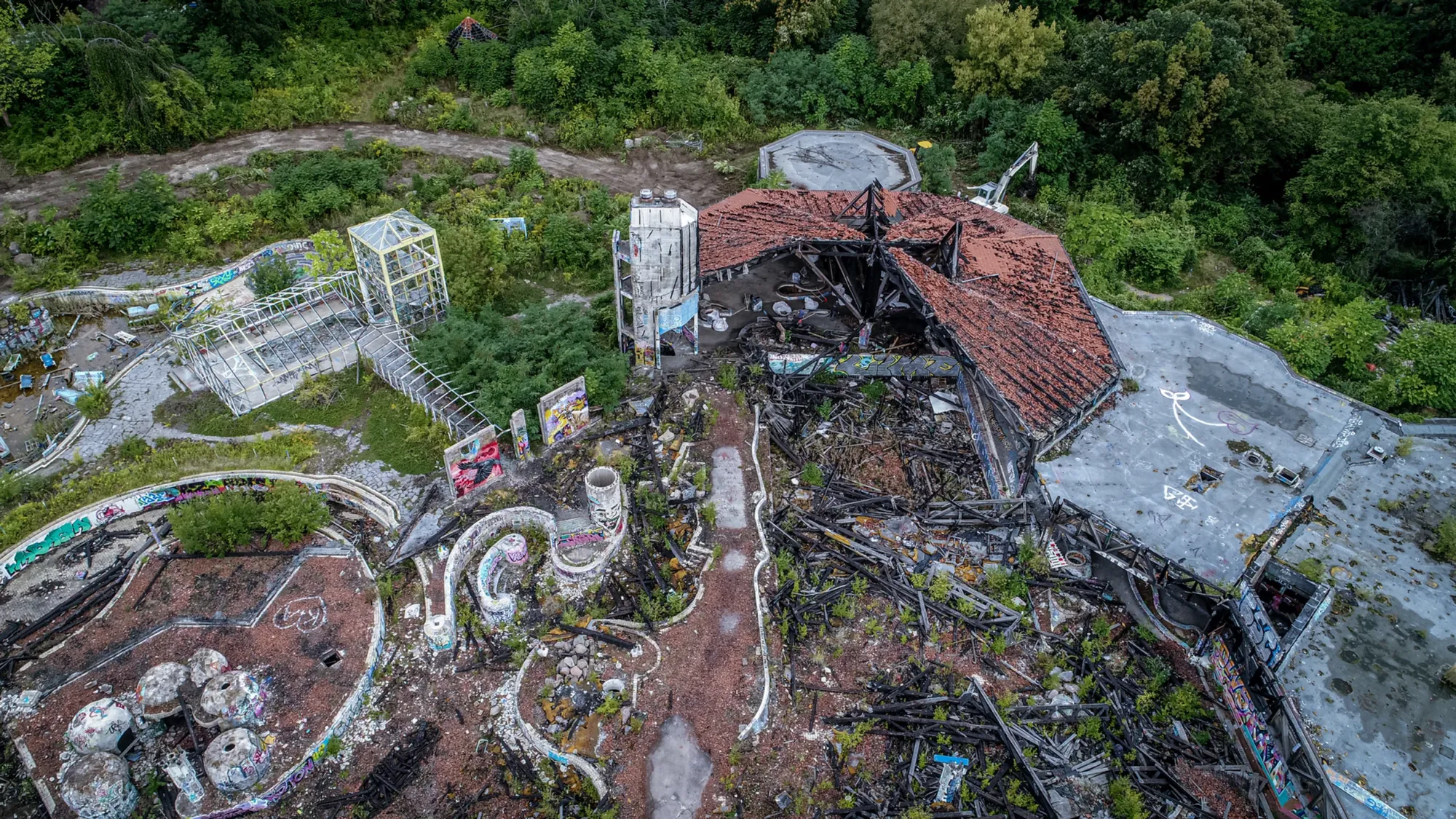 Luftbild vom Rückbau eines verlassenen, überwucherten Gebäudekomplexes im Grünen